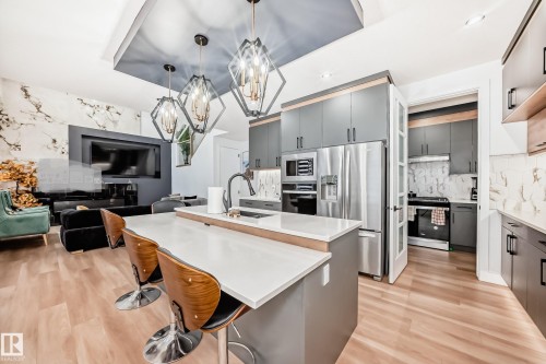 Open concept living area featuring a kitchen island with seating, pendant lighting, stainless steel appliances, and light wood flooring - 15108 11 Street, Edmonton, AB - Indoor Photo Showing Kitchen With Upgraded Kitchen
