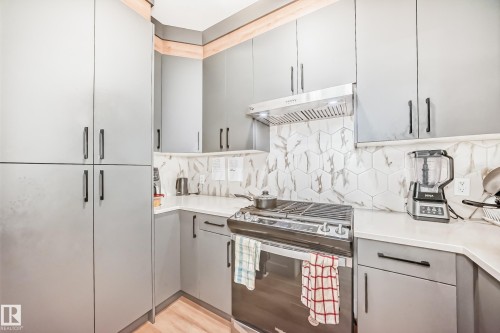 The kitchen features gray cabinetry with dark hardware, a stainless steel range hood, and a white hexagonal tile backsplash - 15108 11 Street, Edmonton, AB - Indoor Photo Showing Kitchen