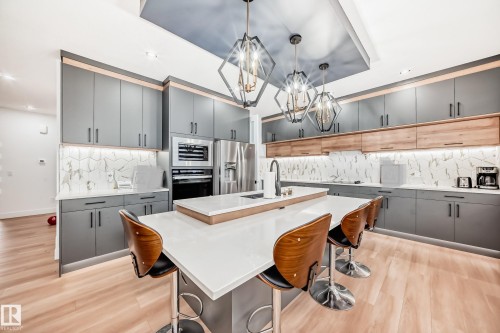 The kitchen features contemporary cabinetry, a central island with seating, a stainless steel refrigerator, and integrated oven - 15108 11 Street, Edmonton, AB - Indoor Photo Showing Other Room