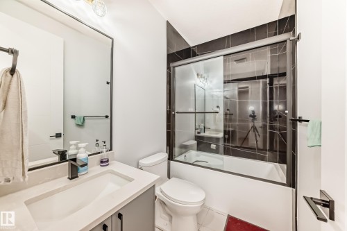 Bathroom featuring a vanity with an integrated sink, a toilet, and a bathtub with a sliding glass shower door - 15108 11 Street, Edmonton, AB - Indoor Photo Showing Bathroom