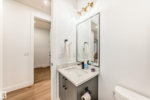 Bathroom featuring a vanity with a light-colored countertop, a rectangular mirror, and a wall-mounted light fixture with gold-toned accents - 15108 11 Street, Edmonton, AB - Indoor Photo Showing Bathroom