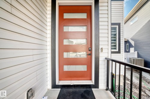 Contemporary entrance featuring a rust-colored door with frosted glass panels, surrounded by white horizontal siding and dark trim - 15108 11 Street, Edmonton, AB - Outdoor With Exterior