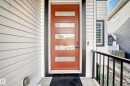 Contemporary entrance featuring a rust-colored door with frosted glass panels, surrounded by white horizontal siding and dark trim - 15108 11 Street, Edmonton, AB  - Outdoor With Exterior 