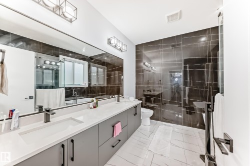 Bathroom featuring a double vanity with matte black faucets, a large mirror, and tiled walls and floors - 15108 11 Street, Edmonton, AB - Indoor Photo Showing Bathroom