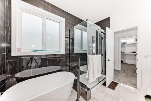 Contemporary bathroom featuring a freestanding tub, a glass-enclosed shower, and dark tiled walls - 15108 11 Street, Edmonton, AB - Indoor Photo Showing Bathroom