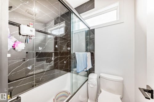 The bathroom features a bathtub and shower combination with dark tiled walls and a clear glass enclosure - 15108 11 Street, Edmonton, AB - Indoor Photo Showing Bathroom