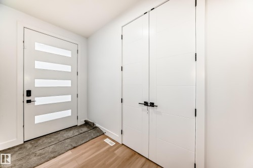 The property features light-toned wood flooring, a white front door with horizontal frosted glass panels, and a white double door with black hardware - 15108 11 Street, Edmonton, AB - Indoor Photo Showing Other Room
