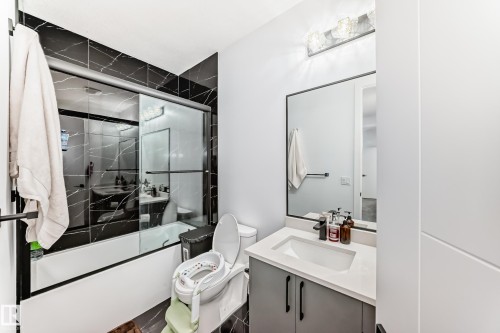 Bathroom featuring black tiled shower walls with white veining, a glass sliding shower door, and a vanity with a white countertop - 15108 11 Street, Edmonton, AB - Indoor Photo Showing Bathroom