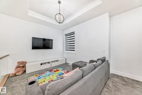 This room features a tray ceiling with a decorative light fixture, carpeted flooring, and a large window with horizontal blinds - 15108 11 Street, Edmonton, AB - Indoor
