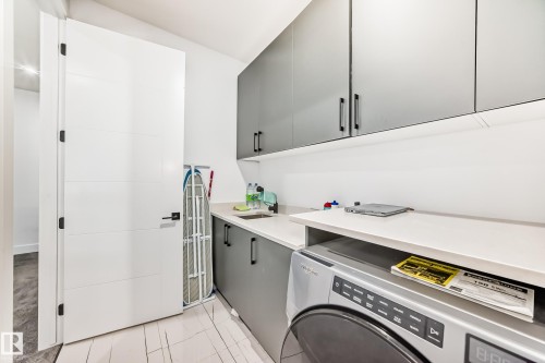 Laundry area featuring a front-load washing machine, extensive countertop space, a sink, and dark gray cabinetry providing ample storage - 15108 11 Street, Edmonton, AB - Indoor Photo Showing Laundry Room
