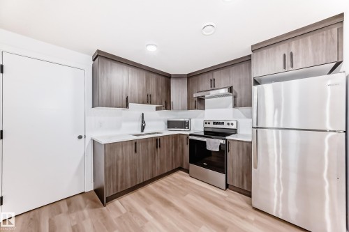 The kitchen features wood-look cabinetry, a light-colored countertop, and a stainless steel refrigerator and oven - 15108 11 Street, Edmonton, AB - Indoor Photo Showing Kitchen