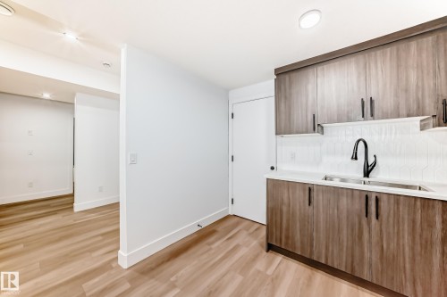 Modern kitchen featuring wood-grain cabinetry, a white tile backsplash, a stainless steel sink with a black faucet, and light-colored flooring - 15108 11 Street, Edmonton, AB - Indoor Photo Showing Kitchen With Double Sink