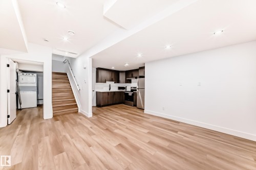 Open concept living space featuring light wood flooring, a modern kitchen with dark cabinetry and stainless steel appliances, and a stacked washer and dryer unit - 15108 11 Street, Edmonton, AB - Indoor Photo Showing Other Room