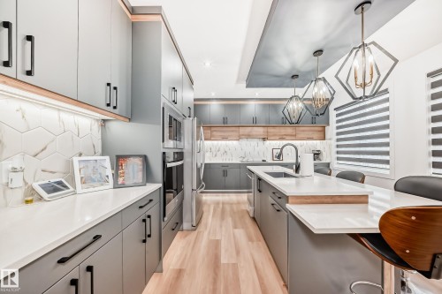 The kitchen features contemporary grey cabinetry with black hardware, light wood flooring, and a central island with a white countertop and seating - 15108 11 Street, Edmonton, AB - Indoor Photo Showing Kitchen With Upgraded Kitchen