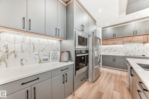 Modern kitchen featuring light hardwood flooring, grey cabinetry with dark hardware, white countertops, and a white and grey hexagonal tile backsplash - 15108 11 Street, Edmonton, AB - Indoor Photo Showing Kitchen With Upgraded Kitchen