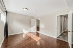 This room features hardwood floors, light-colored walls, and a window with a roller blind and dark curtain - 