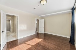 Spacious room featuring rich hardwood flooring, light neutral-toned walls, and a ceiling light fixture - 