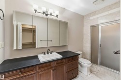 Bathroom featuring a dark wood vanity with a white sink, a large mirror with a four-light fixture, a toilet, and a shower with a frosted glass door - 