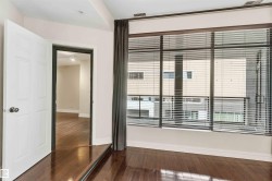 This bedroom features rich hardwood flooring, a large window with horizontal blinds, and a white paneled door - 