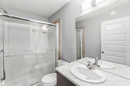 This bathroom features a shower with a sliding glass door, tiled shower surround, a toilet, and a vanity with a white oval sink and a chrome faucet - 1313 Chappelle Boulevard, Edmonton, AB - Indoor Photo Showing Bathroom