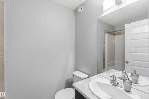 Bathroom featuring a double vanity with two sinks and polished chrome faucets, a toilet, and a shower with beige tiling - 1313 Chappelle Boulevard, Edmonton, AB - Indoor Photo Showing Bathroom