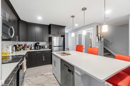 This kitchen features dark wood cabinetry, stainless steel appliances, and a light-colored countertop - 1313 Chappelle Boulevard, Edmonton, AB - Indoor Photo Showing Kitchen With Double Sink With Upgraded Kitchen