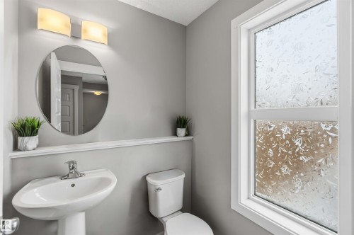 This bathroom features a pedestal sink with a chrome faucet, an oval mirror, and an overhead light fixture with two sconces - 1313 Chappelle Boulevard, Edmonton, AB - Indoor Photo Showing Bathroom