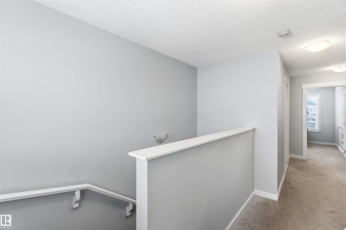 The property features a staircase with a white handrail, leading to a carpeted hallway with light grey walls - 1313 Chappelle Boulevard, Edmonton, AB - Indoor Photo Showing Other Room
