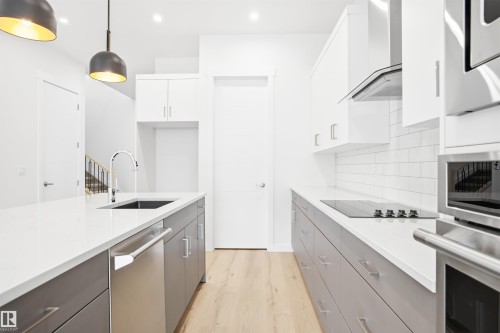 Modern kitchen featuring a large island with a sink, white countertops, and light wood flooring - 9807 90 Avenue, Edmonton, AB - Indoor Photo Showing Kitchen With Upgraded Kitchen