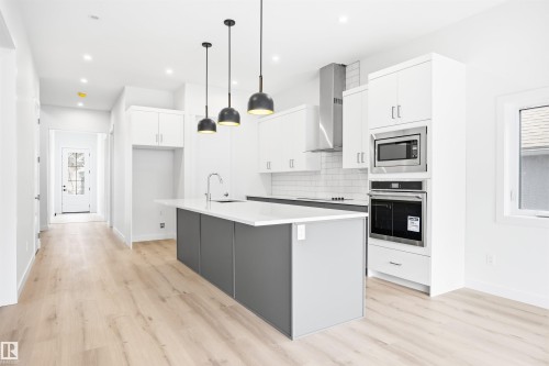 Modern kitchen featuring an island with a sink, stainless steel appliances, white cabinetry, and light-colored flooring - 9807 90 Avenue, Edmonton, AB - Indoor Photo Showing Kitchen With Upgraded Kitchen