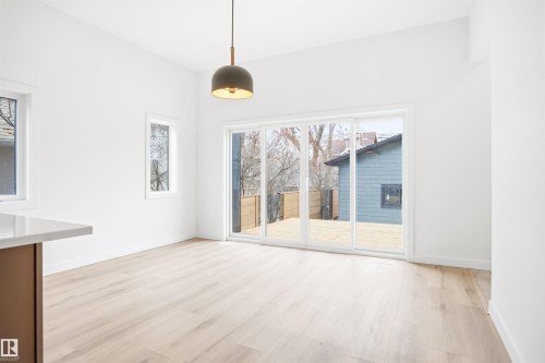 The property features light wood flooring, a modern pendant light fixture, and white walls - 9807 90 Avenue, Edmonton, AB - Indoor Photo Showing Other Room
