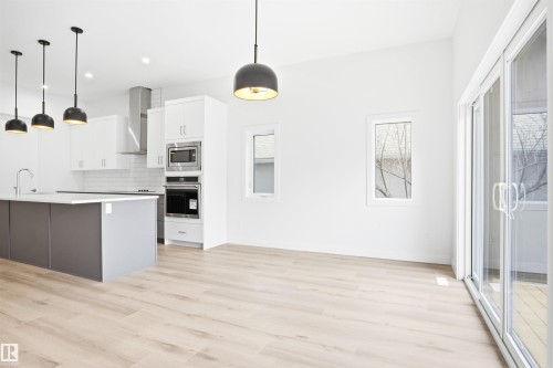 The kitchen features a center island with a sink, white cabinetry, stainless steel appliances, and pendant lighting - 9807 90 Avenue, Edmonton, AB - Indoor Photo Showing Kitchen With Upgraded Kitchen