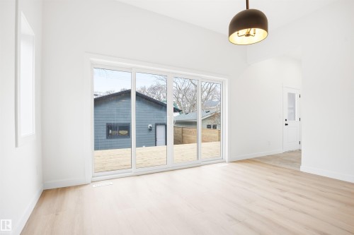 This bright interior space features light-toned hardwood flooring, white walls, and a contemporary light fixture - 9807 90 Avenue, Edmonton, AB - Indoor Photo Showing Other Room