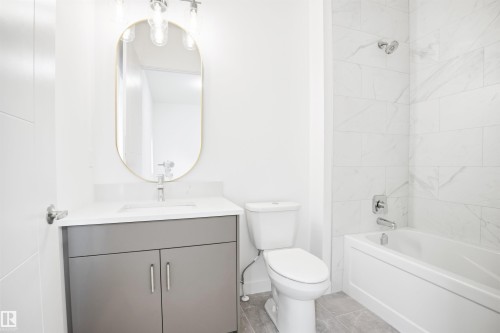 The bathroom features a modern vanity with a rectangular sink, a gold-framed oval mirror, and a white bathtub with subway-style tiled walls - 9807 90 Avenue, Edmonton, AB - Indoor Photo Showing Bathroom