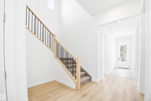 Entryway featuring light-toned hardwood flooring, a staircase with carpeting and modern black balusters, and a white front door with frosted glass - 9807 90 Avenue, Edmonton, AB - Indoor Photo Showing Other Room
