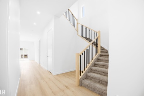 The property features a bright hallway with light-colored flooring and recessed lighting, leading to a carpeted staircase with light wood banisters and black metal spindles - 9807 90 Avenue, Edmonton, AB - Indoor Photo Showing Other Room