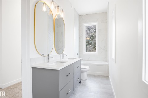 Well-appointed bathroom featuring a double vanity with a light gray cabinet and white countertop, two oval mirrors with gold frames, and a window providing natural light - 9807 90 Avenue, Edmonton, AB - Indoor Photo Showing Bathroom