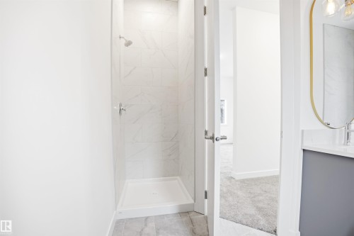 Shower with white tiled walls and a white base, located within a bathroom featuring a vanity with a white countertop and a gold-framed mirror - 9807 90 Avenue, Edmonton, AB - Indoor Photo Showing Bathroom