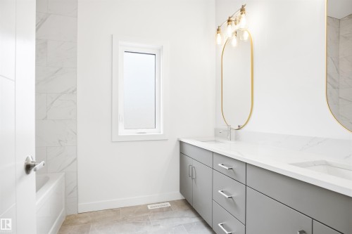 The bathroom features a double vanity with grey cabinetry and white countertops, complemented by oval mirrors and a contemporary light fixture - 9807 90 Avenue, Edmonton, AB - Indoor Photo Showing Bathroom