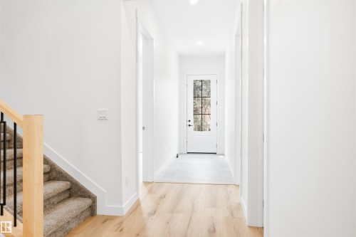 Entryway featuring a light wood floor, a white door with glass panels, and a staircase with light wood banister and black metal spindles - 9807 90 Avenue, Edmonton, AB - Indoor Photo Showing Other Room