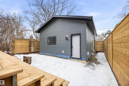 The property features a detached structure with grey siding, a dark roof, and a white door, set within a yard enclosed by a wooden fence - 9807 90 Avenue, Edmonton, AB - Outdoor With Exterior