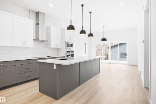 Modern kitchen featuring a large island with a sink, stainless steel appliances, white subway tile backsplash, and light wood flooring - 9807 90 Avenue, Edmonton, AB - Indoor Photo Showing Kitchen With Upgraded Kitchen