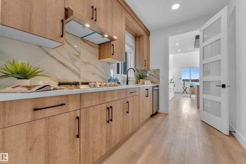 The kitchen features light wood cabinetry with dark hardware, white countertops, a gas cooktop, and a marble-style backsplash - 110 Eldridge Point(E), St. Albert, AB - Indoor Photo Showing Kitchen