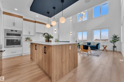 The open concept living area features a kitchen with an island, integrated stainless steel appliances, and light wood flooring - 110 Eldridge Point(E), St. Albert, AB - Indoor Photo Showing Kitchen With Upgraded Kitchen