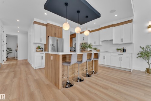 The kitchen features an island with seating for three, a stainless steel refrigerator, and white cabinetry with wood accents - 110 Eldridge Point(E), St. Albert, AB - Indoor Photo Showing Kitchen With Upgraded Kitchen