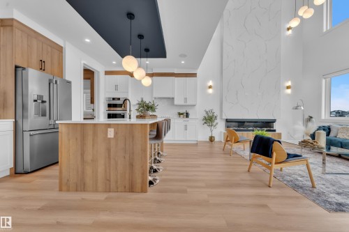 This expansive open-concept living space features light wood flooring throughout, a kitchen island with seating, and a stainless steel refrigerator - 110 Eldridge Point(E), St. Albert, AB - Indoor Photo Showing Kitchen With Upgraded Kitchen