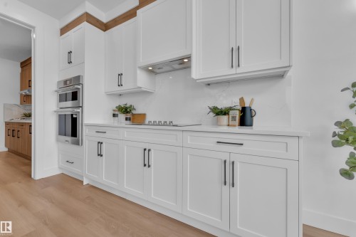 The kitchen features white cabinetry with dark hardware, stainless steel built-in ovens, and light-colored countertops - 110 Eldridge Point(E), St. Albert, AB - Indoor