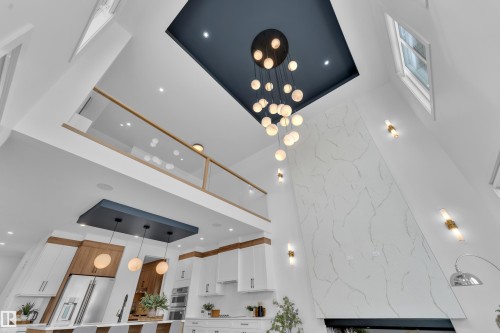 The property features high ceilings with a distinctive dark ceiling accent, a modern chandelier with spherical lights, and a white, marble-patterned accent wall - 110 Eldridge Point(E), St. Albert, AB - Indoor Photo Showing Other Room