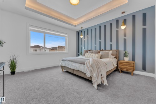 This room features soft gray carpet flooring, a large window providing views of the neighborhood, and a tray ceiling with integrated lighting - 110 Eldridge Point(E), St. Albert, AB - Indoor Photo Showing Bedroom