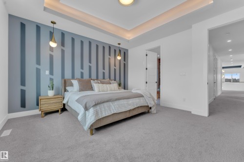 Bedroom featuring light grey carpeting, a tray ceiling with cove lighting, and a decorative accent wall with two pendant lights - 110 Eldridge Point(E), St. Albert, AB - Indoor Photo Showing Bedroom